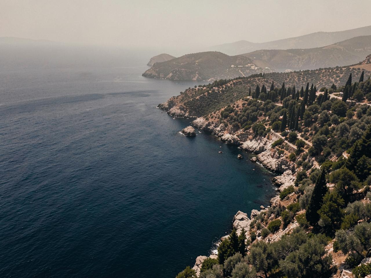Greek coastline with olive and cypress trees above a deep blue bay